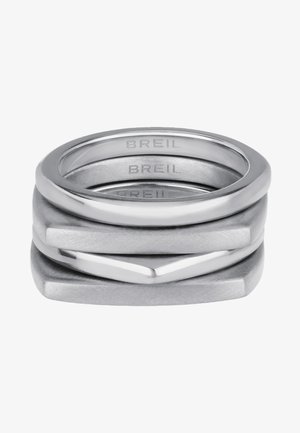 Stos trzech pierścionków wykonanych z metalu srebrnego; cechy obejmują gładkie, polerowane i matowe wykończenia z geometrycznymi kształtami oraz wygrawerowaną nazwą marki.