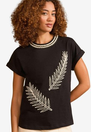 Zwarte katoenen t-shirt met korte opgerolde mouwen, een ronde halslijn met decoratieve afwerking en witte geborduurde varenontwerpen op de voorkant.
