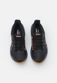 Chaussures de sport noires en matériau synthétique avec une surface texturée, dotées d accents rouges, d un système de laçage et d une semelle en caoutchouc.