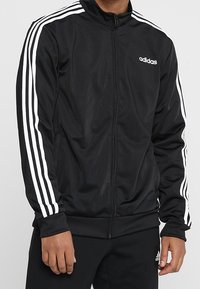 Black zip-up jacket made of smooth fabric, featuring white three-stripe accents on sleeves and a small white logo on the chest.
