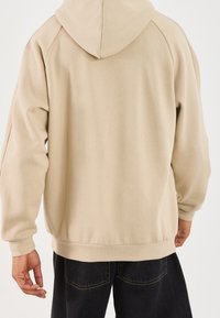 Felpa con cappuccio color beige dal taglio comodo, polsini e orlo a costine, tessuto morbido e design semplice.