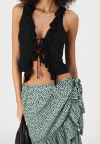 Černý crop top s volánky a vázáním vpředu, doplněný mintově zelenou sukní s černými puntíky a volánkovým lemem.