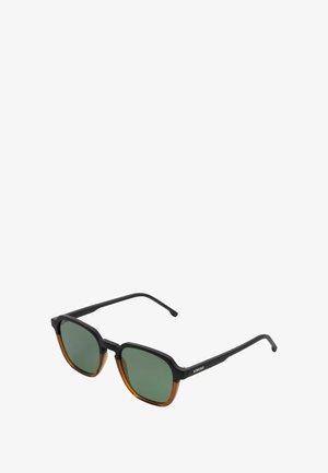 Lunettes de soleil angulaires avec des montures noires et ambres, des verres verts, une texture mate et un logo minimaliste sur la branche noire.