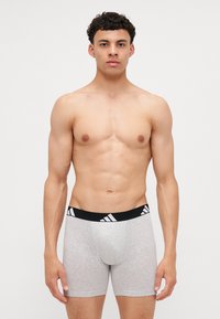 Šedé boxerky s čiernym pásom, ktorý má biele diagonálne pruhy, vyrobené z elastickej bavlnenej zmesi.