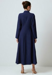 Tumszilti zils garais kleita ar strukturētu apkakli, garām piedurknēm un plūstošu svārku, izgatavots no gludas audi, ar plisējumus aizmugurē.