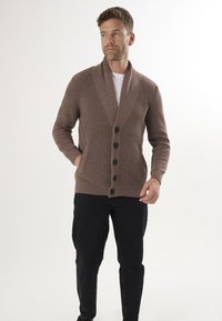 Pruneeritud kardigan, millel on kaelarätt, sooniline tekstuur ja kuus musta nööpi. Kanda valge T-särgi ja mustade pükstega.