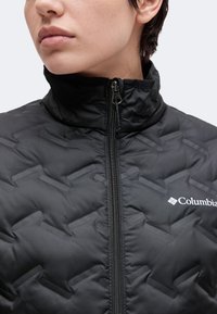 Gros plan d'une personne portant une veste noire Columbia avec une fermeture éclair visible et un col montant.