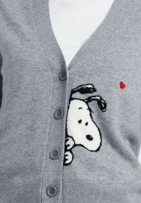 Grijze cardigan van zachte stof, met een cartoon hondenontwerp in zwart-wit en een rood hart. Vijf grijze knopen aan de voorkant.