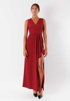 Lungo abito bordeaux con scollatura a V profonda, senza maniche e uno spacco fino alla coscia; realizzato in un tessuto liscio. Indossato con tacchi neri.