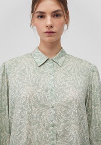 Light green button-up shirt made of soft fabric, featuring a delicate white leaf pattern, classic collar, and rounded button closures.