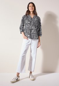 Blusa de patrón blanco y negro con escote en V y mangas tres cuartos, combinada con pantalones anchos blancos y zapatillas blancas.