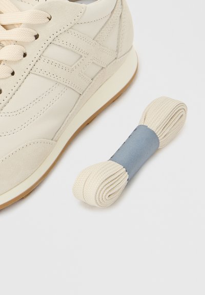 Υποπίνακας εκρού με σουέτ διακοσμήσεις και υφή στην πλαϊνή σχεδίαση, συνοδευόμενος από ρολάρισμένο δεματάκι από εκρού κορδόνια στο ίδιο χρώμα με μπλε λωρίδα.