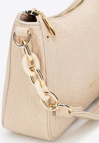 Sac à main en cuir texturé beige avec une fermeture éclair dorée. Présente une chaîne décorative avec des maillons couleur crème et des coutures blanches contrastées.