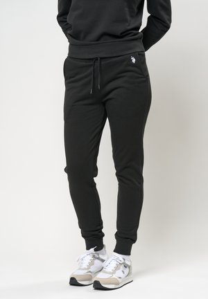 Zwarte joggingbroek met een elastische tailleband en touwtje, met zijzakken en een klein logo op de linker heup, gecombineerd met sneakers.