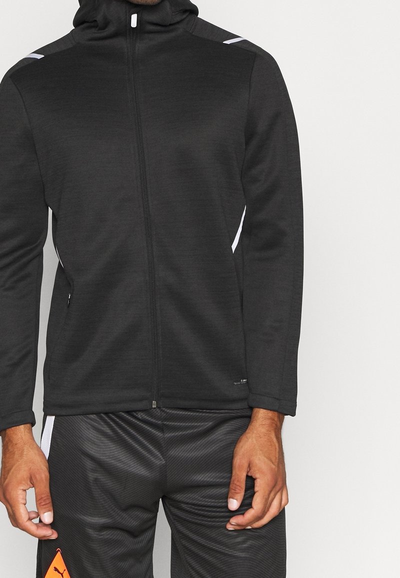 Schwarze Zip-Hoodie aus strukturiertem Stoff, mit hohem Kragen, weißen Akzenten auf den Schultern und schlanker Passform.