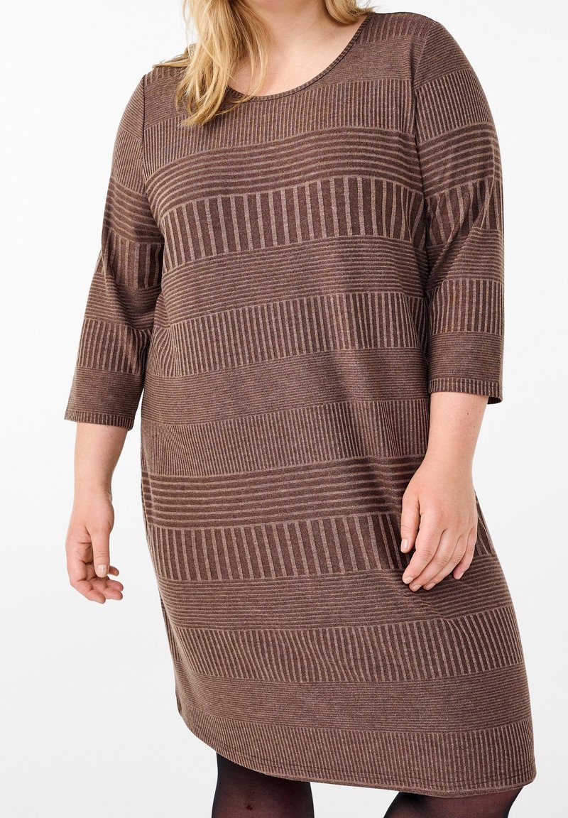 Femme portant une robe marron rayée, longueur genou, avec des manches trois-quarts sur fond blanc.
