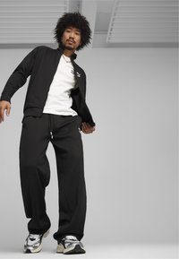 Svart zip-jacka med hög krage, vit T-shirt och löst sittande svarta byxor. Modellen har på sig vita och svarta sneakers.