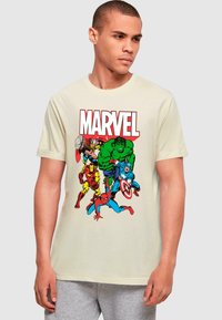 Kreminės spalvos marškiniai trumpomis rankovėmis, ant kurių pavaizduoti Marvel komiksų herojai: Hulkas, Geležinis žmogus, Thoras, Kapitonas Amerika ir Žmogus voras, ryškiomis spalvomis.
