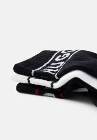 Calcetines de cuadro en blanco y negro apilados, con textura acanalada, rayas en contraste y detalle del logo en rojo.