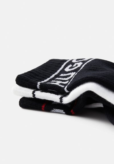 Chaussettes de crew en noir et blanc empilées, avec une texture côtelée, des rayures contrastées et un détail de logo en rouge.