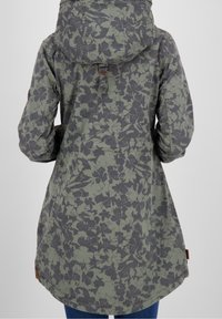 Parka verde oliva con estampado floral y capucha, que presenta un detalle de hebilla en la parte posterior y bolsillos laterales, fabricada con una tela texturizada.