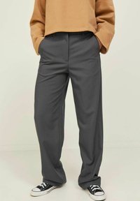 Grijze wijde broek met voorplooien, gemaakt van een gladde stof. Gecombineerd met zwart-witte sneakers en een bruin cropped sweatshirt.