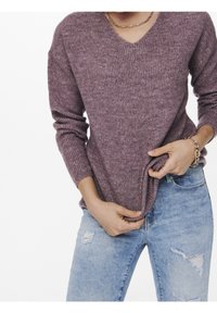 Sweter z dekoltem w serek, w żebrowanym splocie, w kolorze mauve, z długimi rękawami i luźnym krojem, w połączeniu z przetartymi jasnoniebieskimi dżinsami.