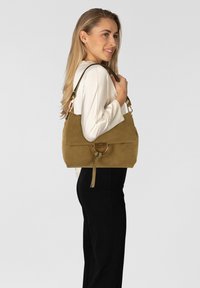 Borsa a mano in camoscio verde oliva con design strutturato, caratterizzata da un anello dorato e tracolla removibile. Texture liscia e chiusura minimalista.