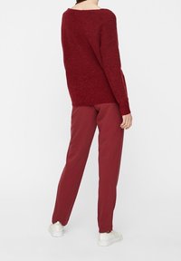 Bordowy, oversize sweter z dzianiny z szerokim dekoltem, połączony z dopasowanymi spodniami, zakończony białymi sneakersami. Miękka faktura.