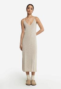 Beżowa, dziana sukienka maxi z szerokim dekoltem w kszta�łcie litery V i cienkimi, regulowanymi ramiączkami. Połączona z jasnymi skarpetkami i beżowymi butami wsuwanymi.
