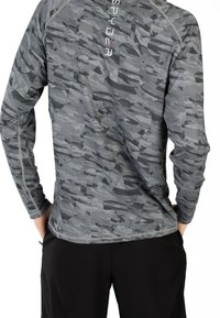 Giacca grigia a maniche lunghe con un motivo camouflage geometrico, tessuto testurizzato e cuciture a contrasto lungo le spalle e i lati.