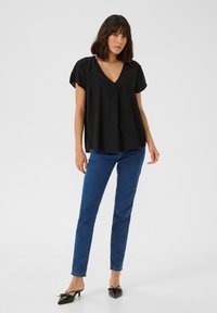 Black short-sleeve blouse with a V-neckline, loose fit, and lightweight fabric. Worn with blue jeans and black pointed-toe heels.