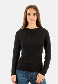 Maglia nera a maniche lunghe con una finitura testurizzata e scintillante; scollatura tonda; design aderente abbinato a jeans in denim blu.