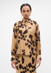 Bruine en beige langemouw shirt met een kraag en een zwart abstract panterprint patroon. Zachte stof met een ontspannen pasvorm.