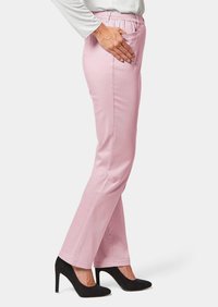 Roze broeken met een elastische tailleband, rechte pijpen en zijzakken, gecombineerd met zwarte hoge hakken. Glad textuur.