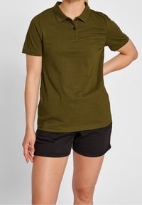 Oliven grøn polo-shirt med krave, korte ærmer og tre knapper. Båret med sorte shorts, glat stoftekstur.
