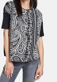 Czarnobiała koszulka z krótkim rękawem, ozdobiona misternymi wzorami paisley oraz geometrycznymi akcentami na teksturowanej tkaninie.