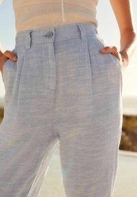 Lichtblauwe linnen broek met een ontspannen pasvorm, voorzien van een enkele knoopsluiting, zijzakken en subtiele textuurvariaties.