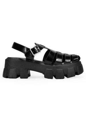 Sandalias negras de tacón ancho con diseño de parte superior trenzada, que cuentan con una correa con hebilla y suela de goma gruesa con formas de bloque distintivas.