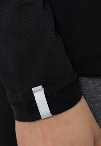 Maglia sportiva nera a maniche lunghe con una forma aderente, texture liscia e una piccola etichetta bianca di tessuto vicino al polsino. Adatta per l'abbigliamento attivo.