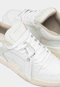 Sneakers bianchi con pelle testurizzata e accenti in suede, caratterizzati da una punta perforata, lacci piatti e un'etichetta metallica con il marchio.