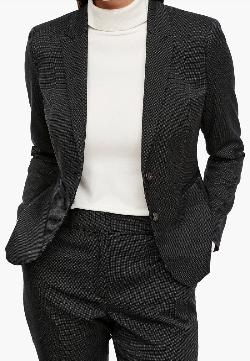 Czarna marynarka o fakturze, dopasowana, z klapami, na dwa guziki i pasującymi spodniami. Noszona na białym golfie.