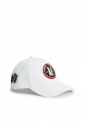 Gorra de béisbol blanca con parche circular del logo de Tommy Hilfiger en la parte delantera y "85" bordado en negro y rojo en el lateral.