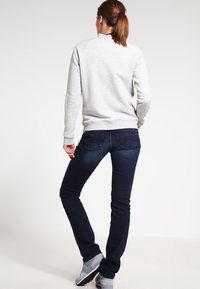Grijze sweatshirt met geribde onderkant en mouwen, gecombineerd met donkerblauwe skinny jeans. Sneakers met een gestructureerde zool maken het outfit af, gezien van achteren.