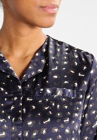 Blusa blu navy con motivo leopardato in marrone e bianco, con colletto e taschino sul petto, realizzata in un morbido tessuto di raso.