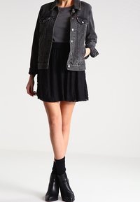 Veste en denim noir portée sur un haut gris, associée à une jupe évasée noire. Comprend des bottines noires mi-cheville et des chaussettes noires pour créer du contraste.