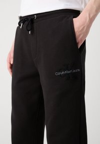 Zwarte trainingsbroek met een elastische tailleband, trekkoord, zijzakken en geborduurd "Calvin Klein Jeans" logo op het been. Zachte stof.