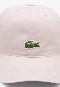 Šviesiai rožinė beisbolo kepuraitė iš tekstūruotos medžiagos su išsiuvinėtu žaliu krokodilo logotipu priekyje. Skydelis su siūlėmis.
