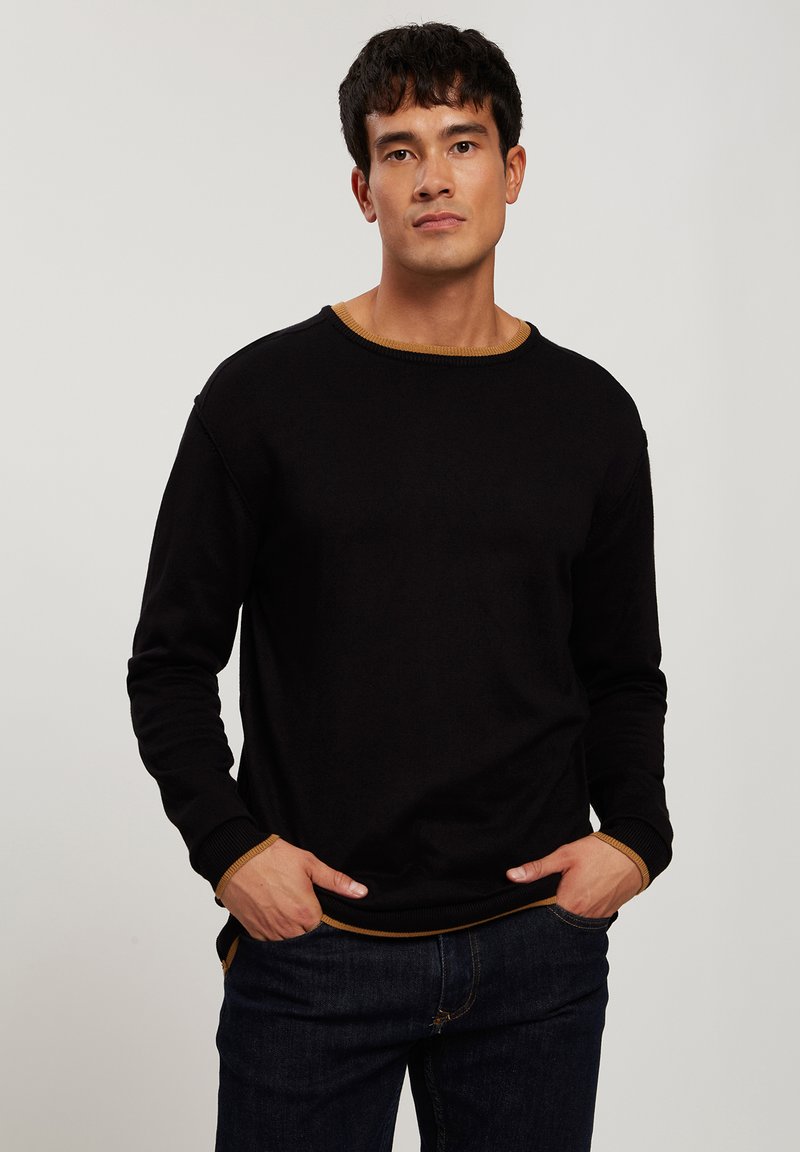 Czarny sweter z okrągłym dekoltem, długimi rękawami i kontrastowym złoto-brązowym wykończeniem przy kołnierzu i mankietach; gładka tekstura.