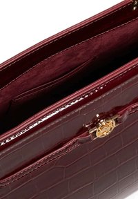 Burgundy patent leather handbag with crocodile texture, featuring a gold-tone logo hardware and a suede-lined interior pocket.